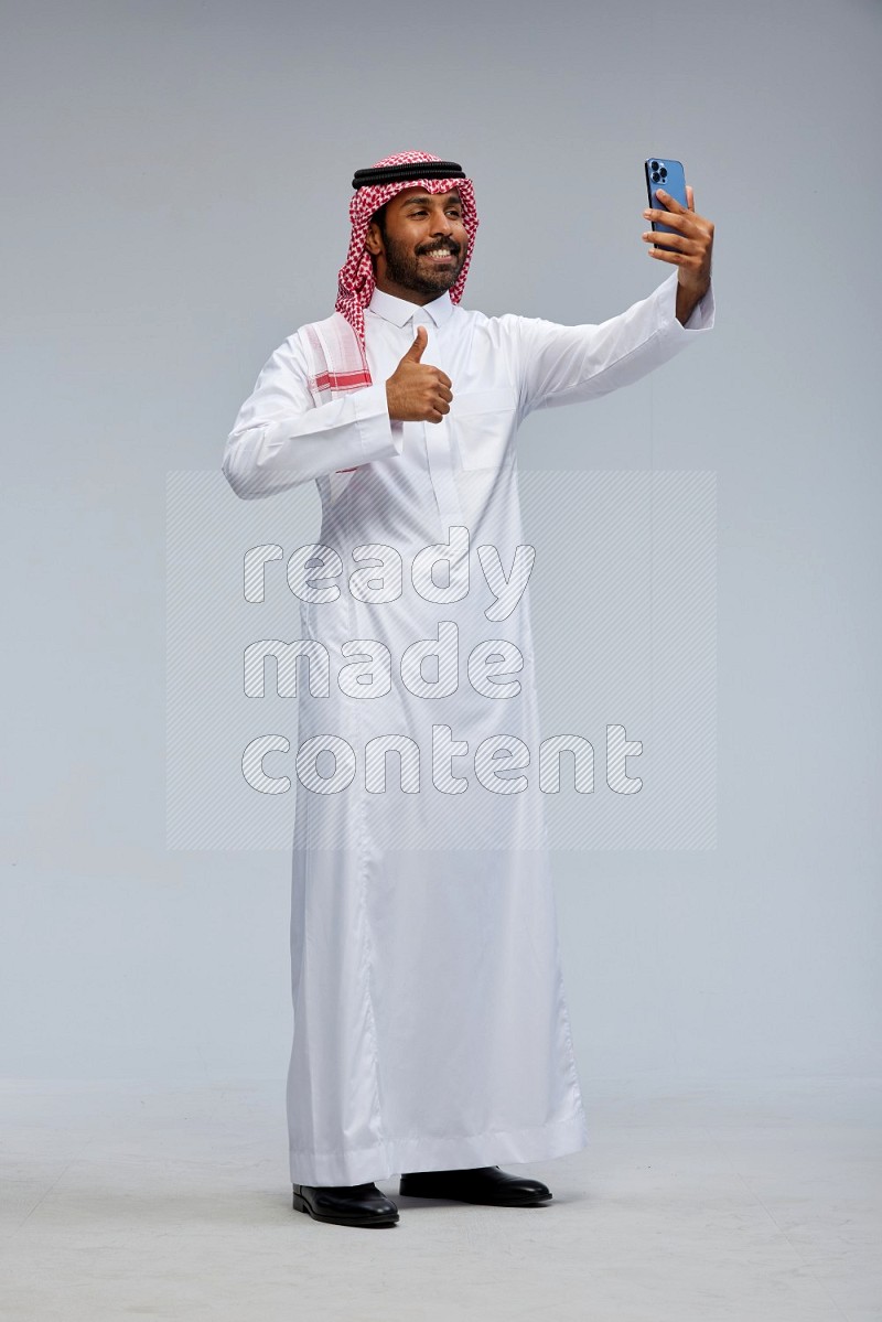 Saudi man Wearing Thob and shomag standing taking selfie on Gray background