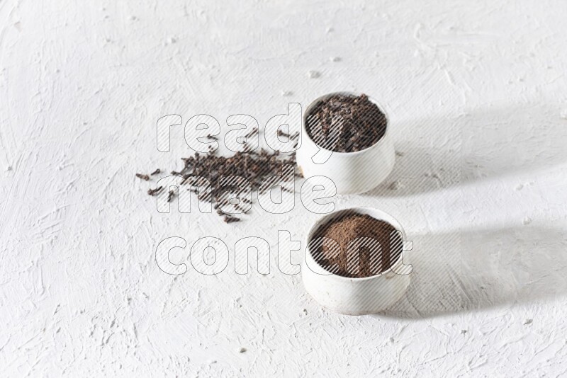 2 Beige ceramic bowls, one full of cloves and the other full of powder on textured white flooring