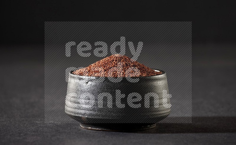 A black pottery bowl full of garden cress seeds on a black flooring