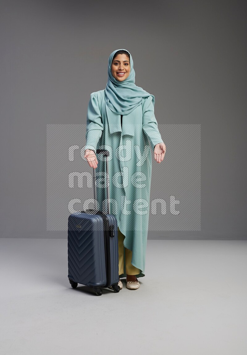 Saudi Woman wearing Abaya standing holding Travel bag on Gray background