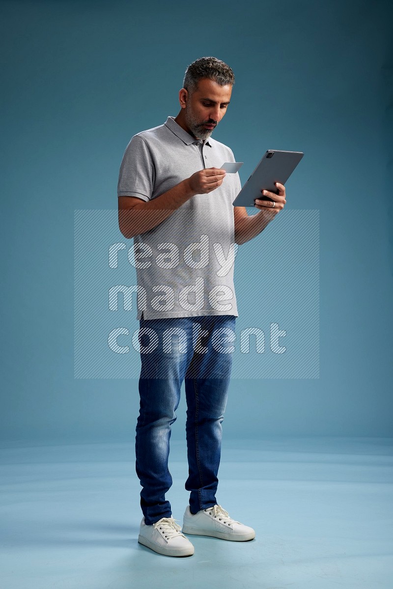 Man Standing holding ATM while working on tablet on blue background