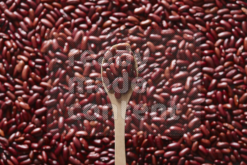 A wooden spoon full of red kidney beans on red kidney beans background