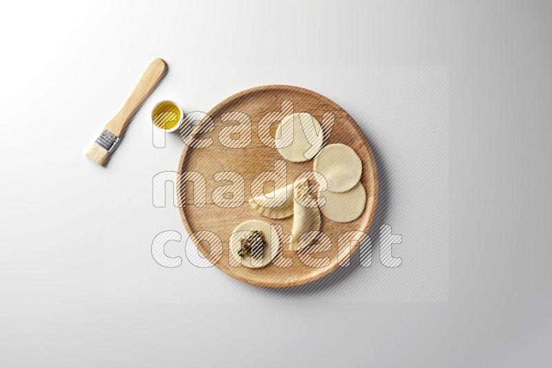two closed sambosas and one open sambosa filled with meat while oil with oil brush aside in a wooden dish on a white background