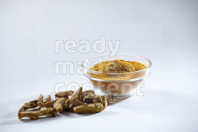 A glass bowl full of turmeric powder and dried whole fingers beneath it on white flooring