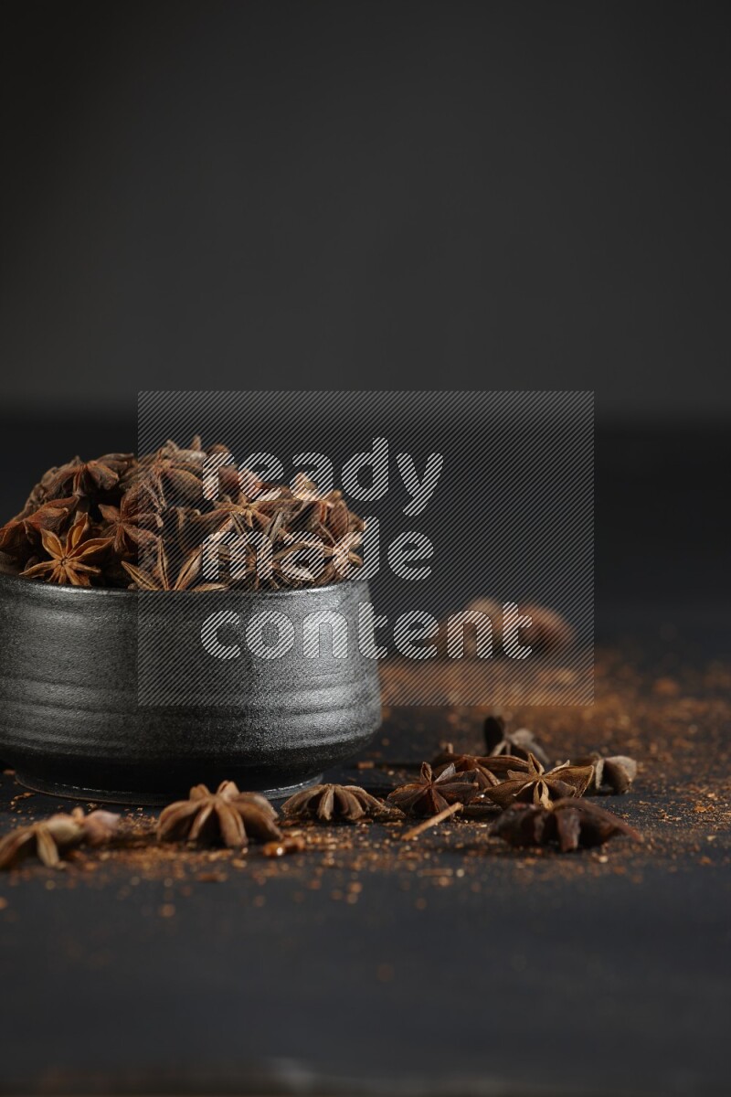 Star Anise in a black bowl with sprinkled anise on black flooring