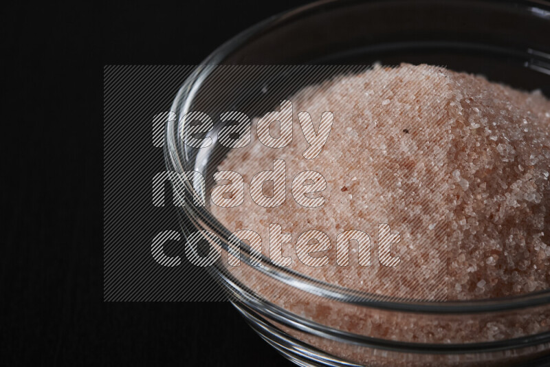 A glass bowl full of fine himalayan salt on black background