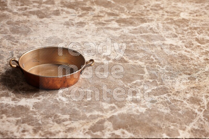 A small copper pan on beige marble background