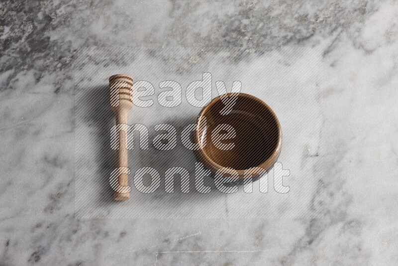 Brown pottery bowl with wooden honey dipper on the side on grey marble background