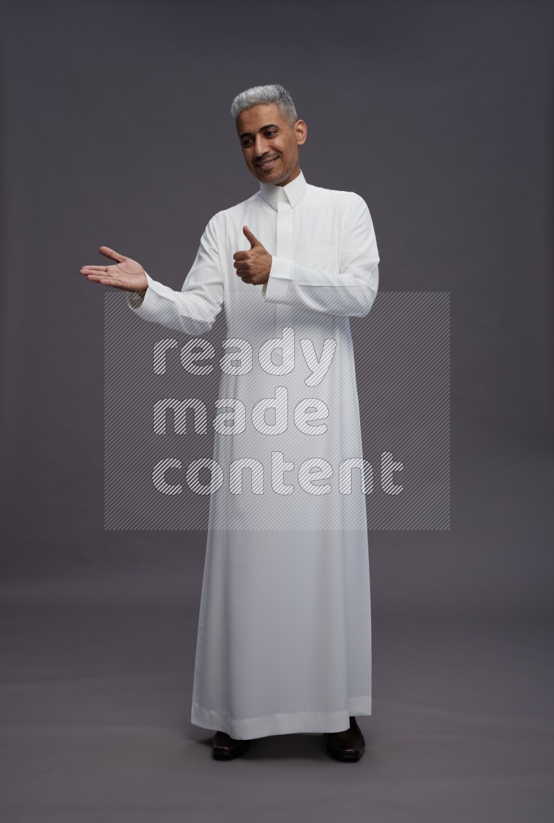 Saudi man wearing thob standing interacting with the camera on gray background