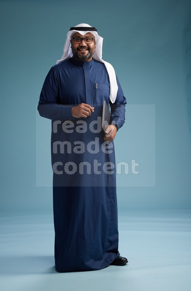Saudi Man with shimag Standing working on laptop on blue background