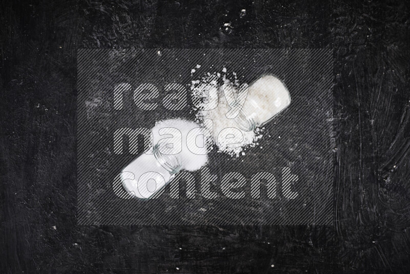 2 glass jars one is filled with table salt and the other with coarse sea salt on black background