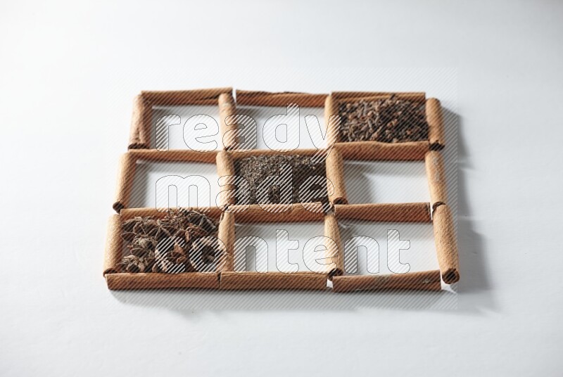 9 squares of cinnamon sticks full of tea in the middle surrounded by nutmeg, dried mint, cloves, dried basil, dried ginger, cinnamon, star anise and cardamom on white flooring