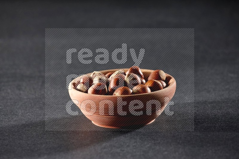 A wooden bowl full of hazelnuts on a black background in different angles