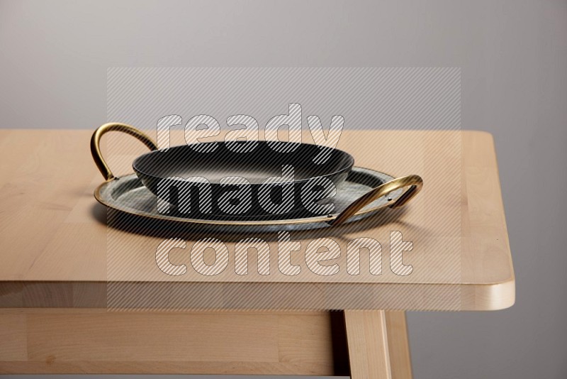 black plate placed on a rounded stainless steel metal tray with golden handels on the edge of wooden table