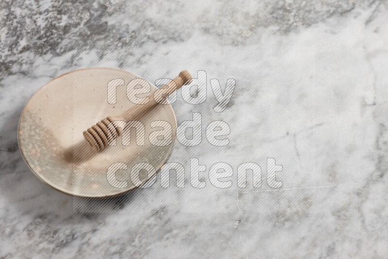 Multicolored pottery plate with wooden honey dipper in it on grey marble background