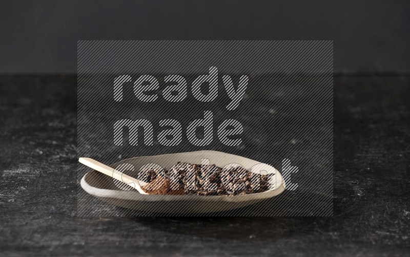 A Pottery plate full of cloves and a wooden spoon full of cloves powder on it on a textured black background