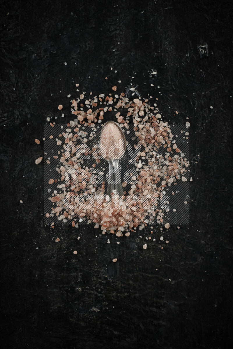 2 metal spoons filled with pink himalayan salt on black background