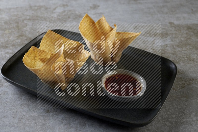 wonton cups with soy sauce ramkin on rectangle dark grey ceramic plate on grey textured counter top