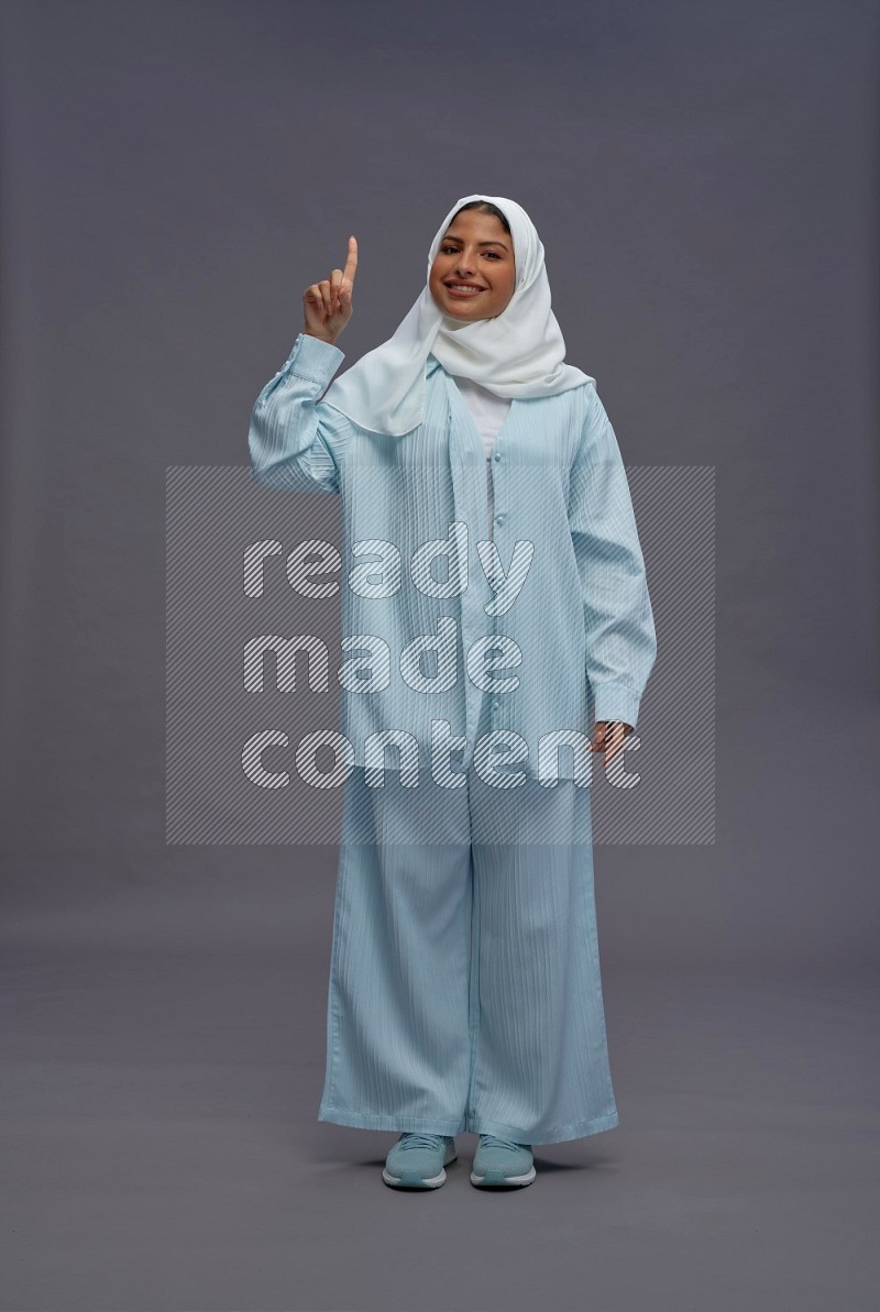 Saudi woman wearing hijab clothes standing interacting with the camera on gray background