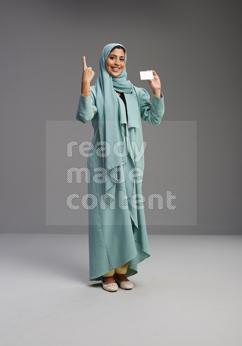 Saudi Woman wearing Abaya standing holding ATM card on Gray background