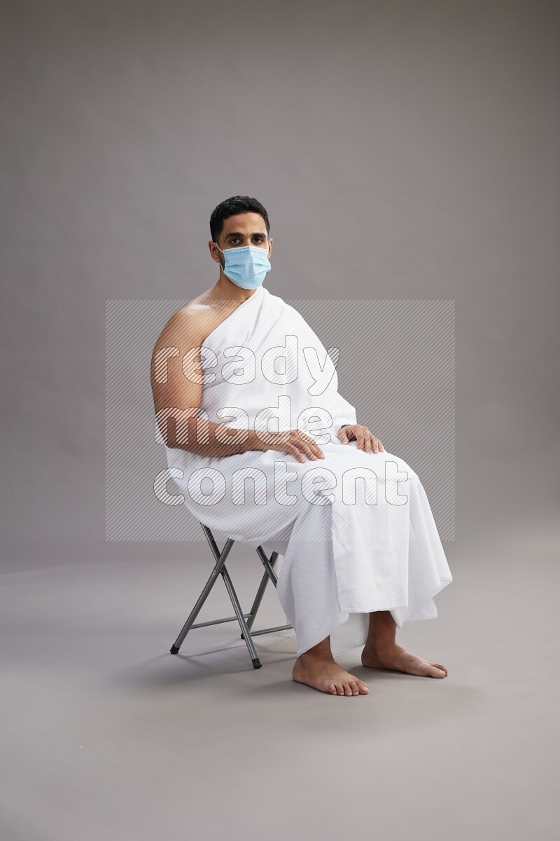 A man wearing Ehram with face mask sitting on chair Interacting with the camera on gray background