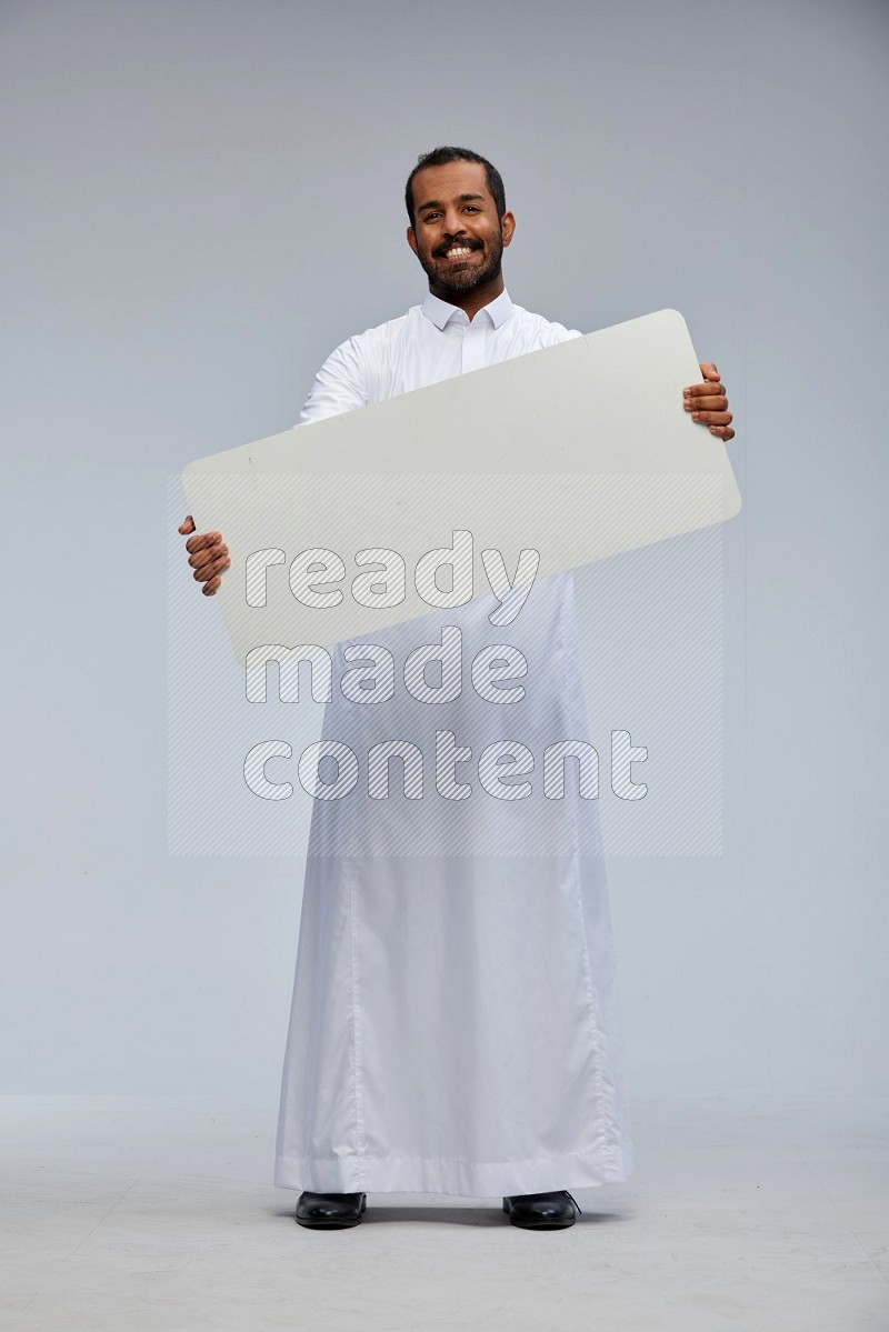 Saudi man wearing Thob standing holding board on Gray background