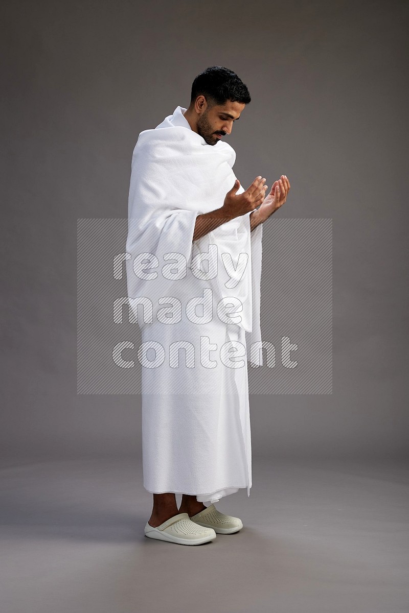 A man wearing Ehram Standing performing dua'a on gray background