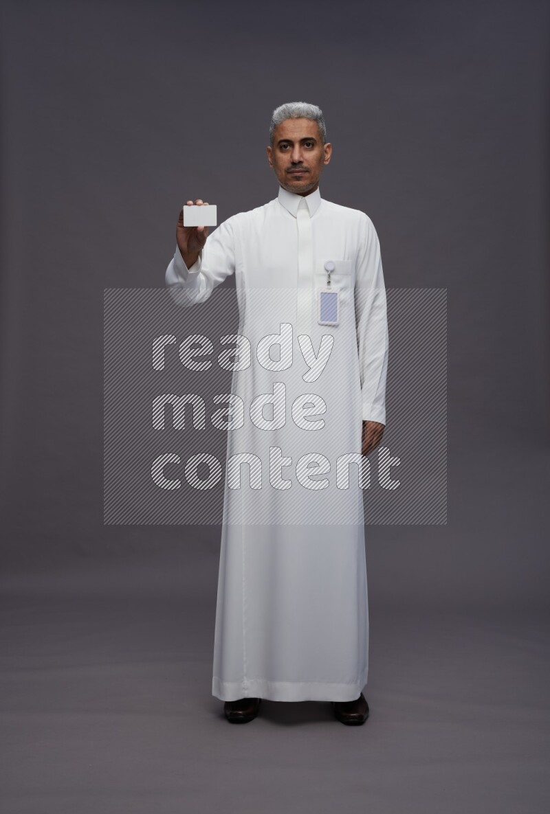 Saudi man wearing thob with pocket employee badge standing holding ATM card on gray background
