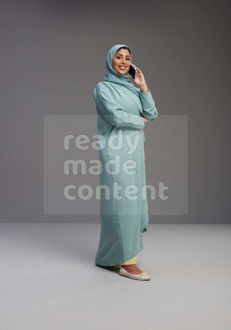 Saudi Woman wearing Abaya standing talking on phone on Gray background