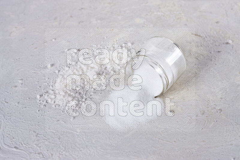 A glass jar full of table salt with some sea salt crystals beside it on a white background