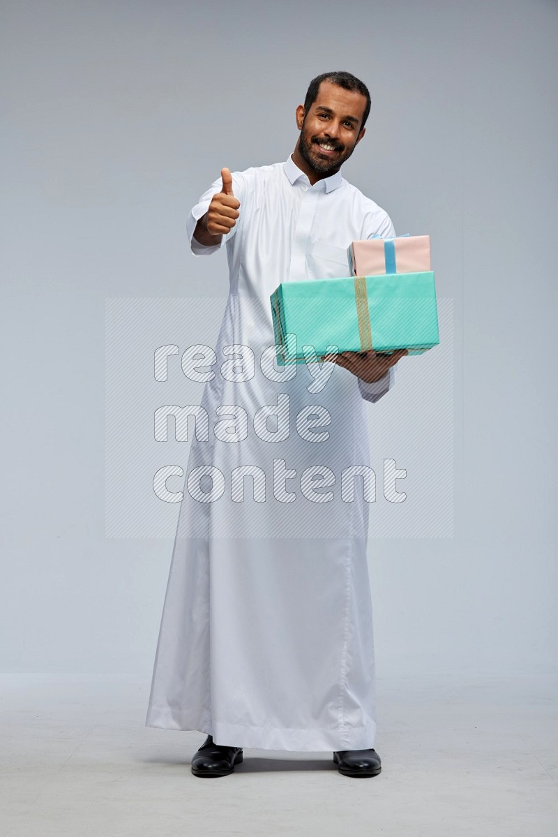 Saudi man Wearing thob standing holding gift box on Gray background