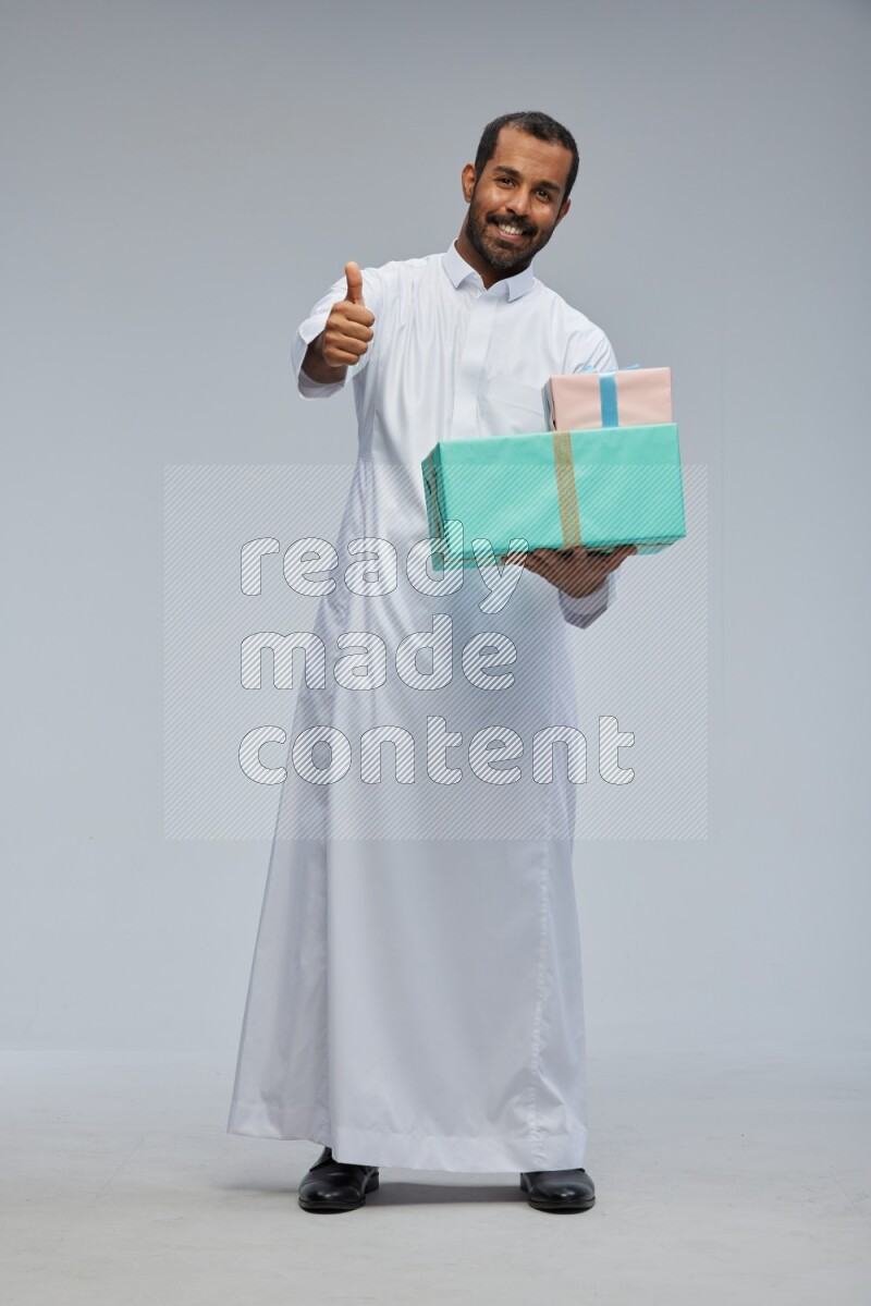 Saudi man Wearing thob standing holding gift box on Gray background