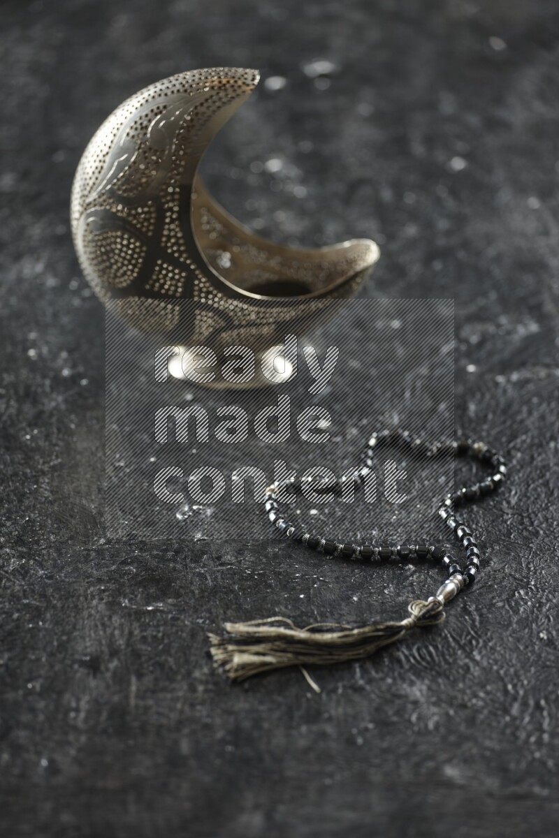 A silver lantern with different drinks, dates, nuts, prayer beads and quran on textured black background