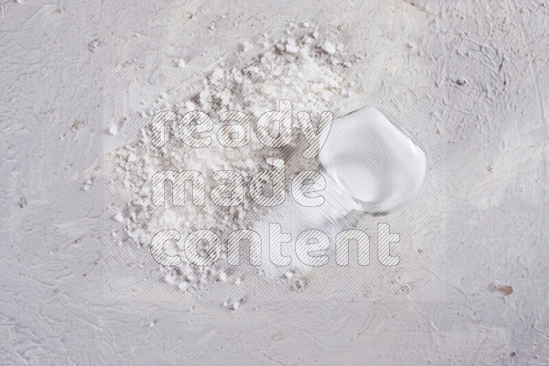 A glass jar full of table salt with some sea salt crystals beside it on a white background