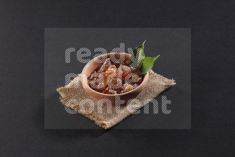 A wooden bowl full of gum arabic on a piece of burlap on black flooring