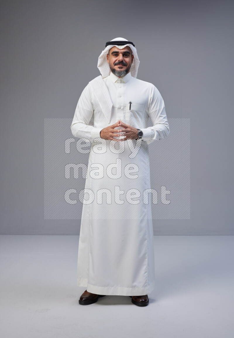 Saudi man Wearing Thob and white Shomag standing interacting with the camera on Gray background