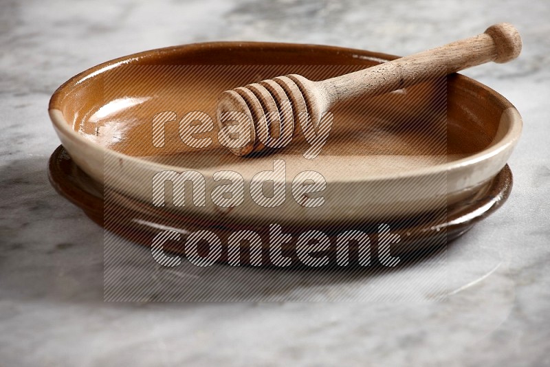 Multicolored Pottery Oven Plate with wooden honey handle in it, on grey marble flooring, 15 degree angle