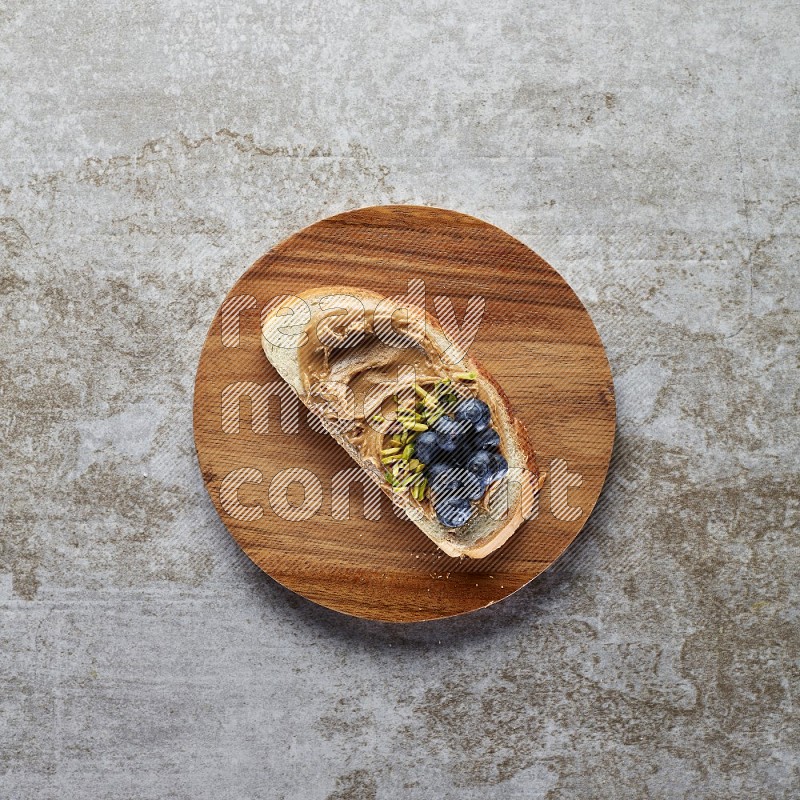 open faced peanut butter sandwich with blueberries and pistachio on a grey textured background