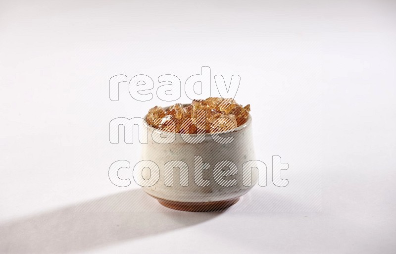 A beige pottery bowl full of gum arabic on white flooring
