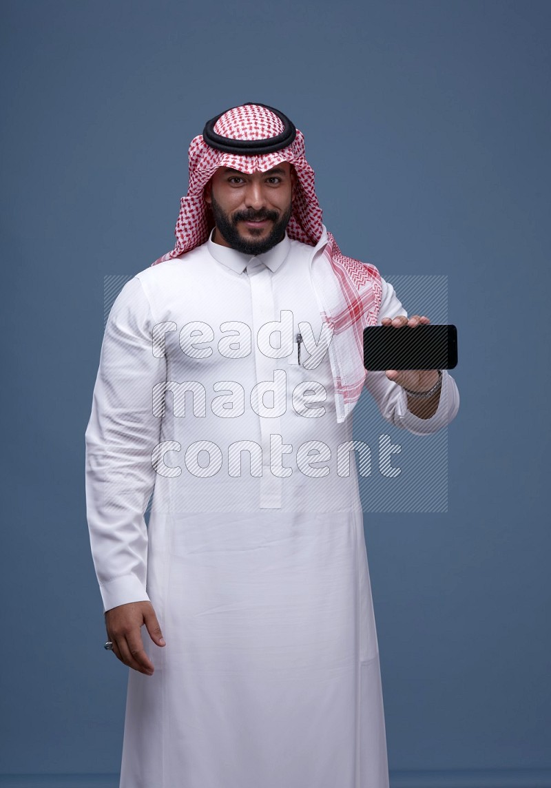 A man Showing his smartphone Screen on Blue Background wearing Saudi Thob