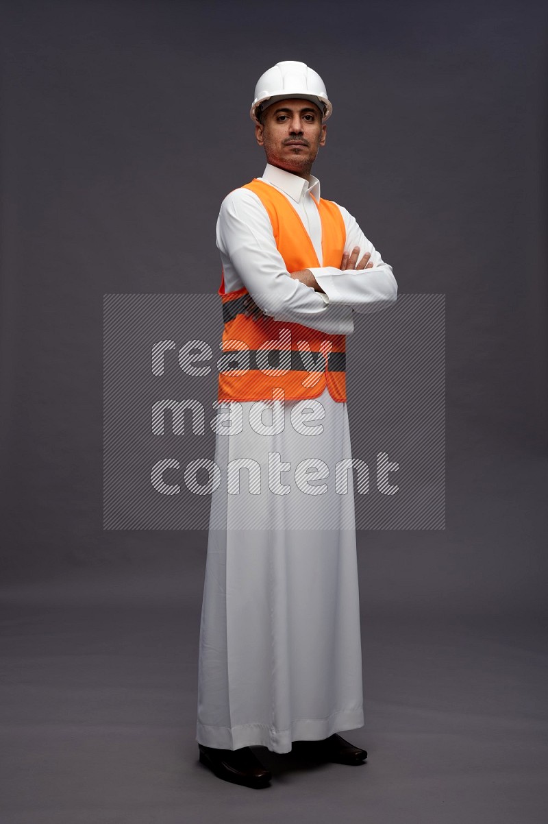 Saudi man wearing thob with engineer vest standing with crossed arms on gray background