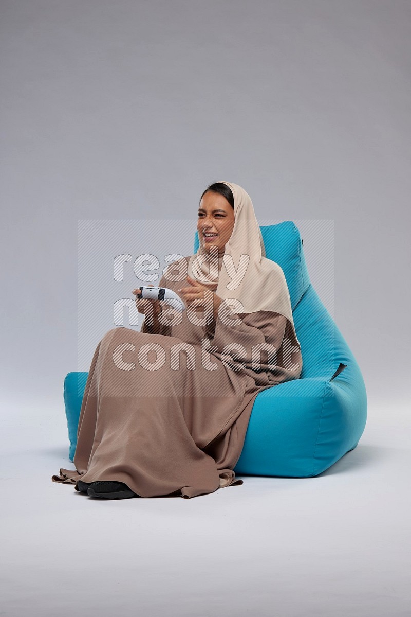 A Saudi woman sitting on a blue beanbag and gaming with joystick