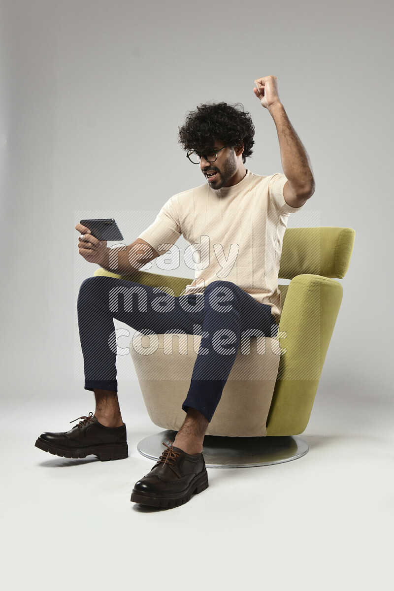 A man wearing casual sitting on a chair gaming on the phone on white background