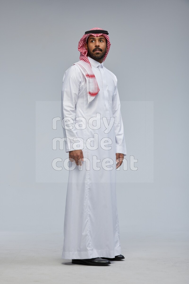 Saudi man Wearing Thob and shomag standing interacting with the camera on Gray background