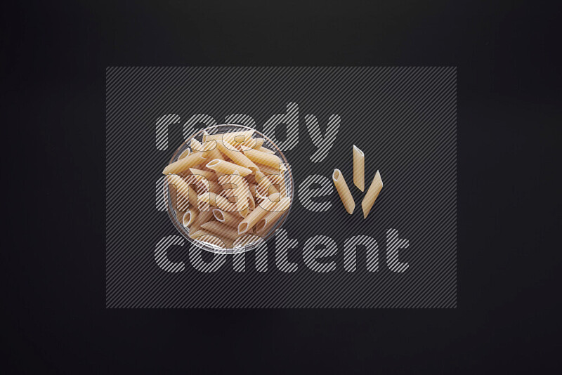 Penne pasta in a glass bowl on black background