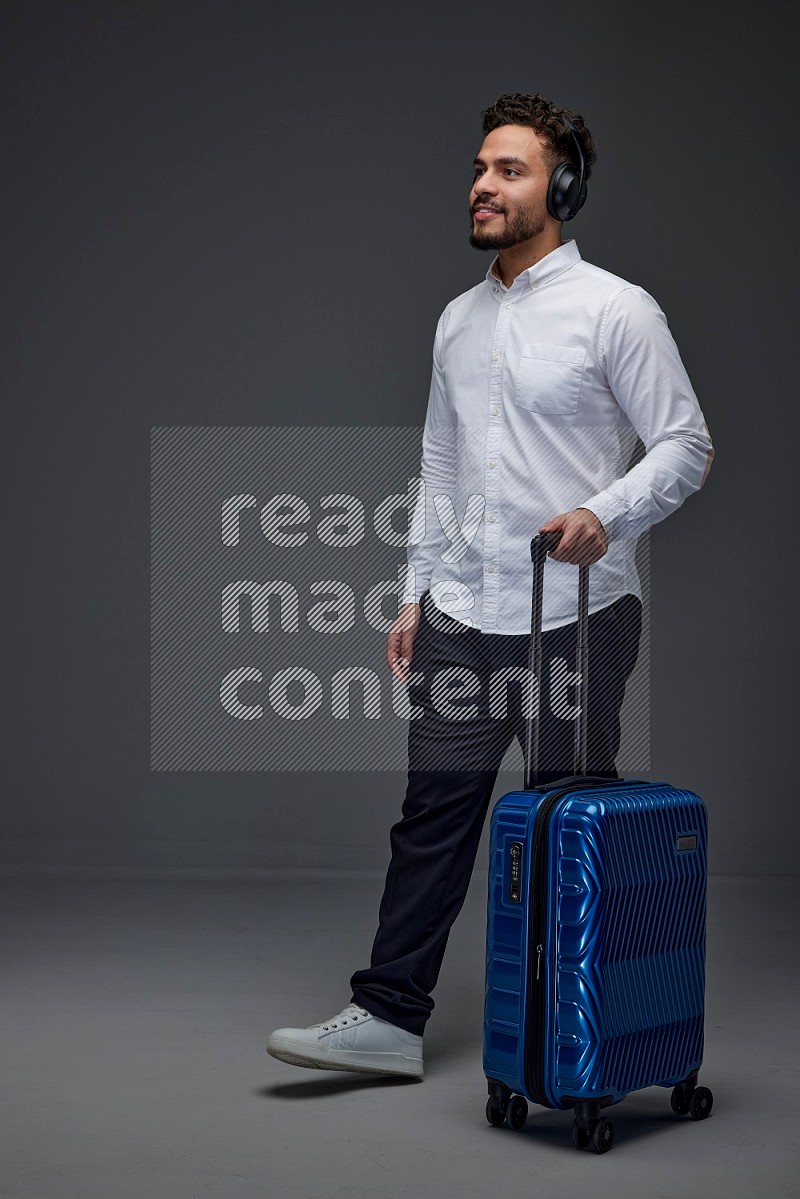 A man Posing with a carry-on with headsets  Wearing a White shirt on a grey background