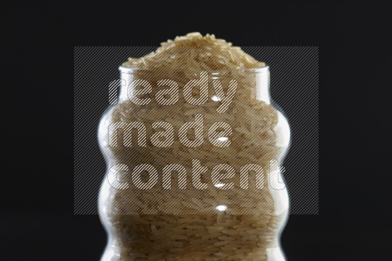 Basmati golden rice in a glass jar on black background