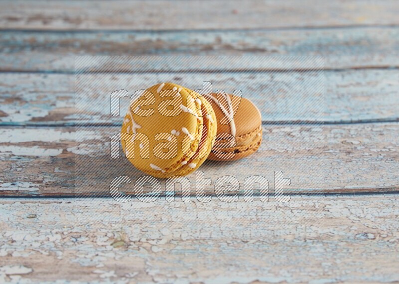 45º Shot of of two assorted Brown Irish Cream, and Yellow Piña Colada macarons on light blue background