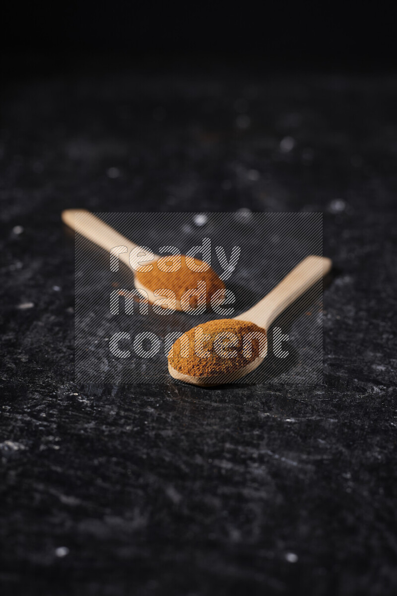 Two wooden spoons full of ground paprika powder on black background