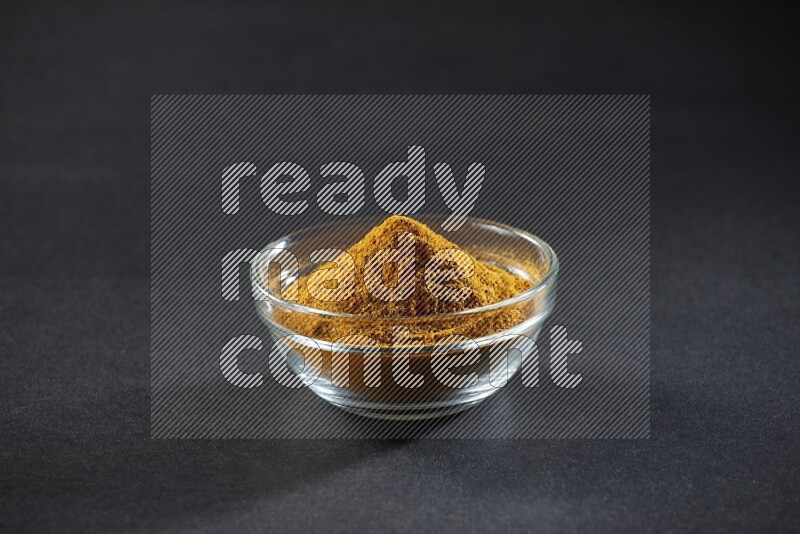 A glass bowl full of turmeric powder on black flooring
